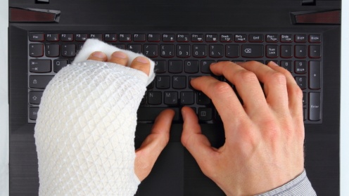 Zwei Hände auf Laptop-Tastatur, eine davon mit Gipsschiene
