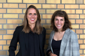 Sophie Kazmierczak und Tanja Volksheimer von der Bundesinitiative Impact Investing vor einer gelben Backstein-Wand..