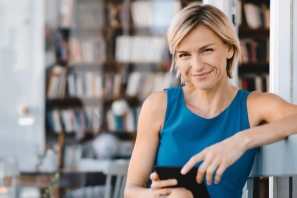 Bild einer lächelnden Frau mit Smartphone vor Bücherwand