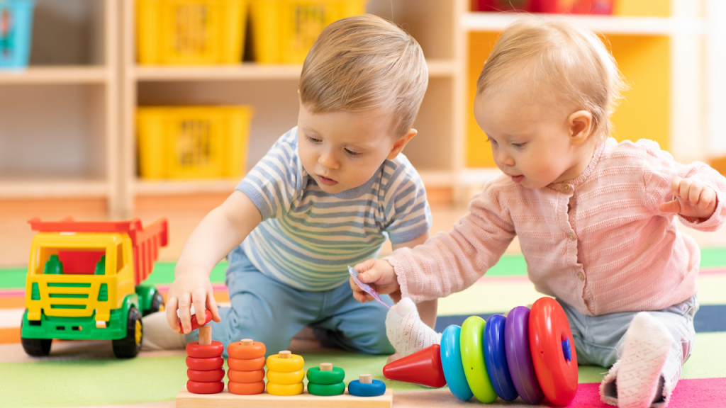 Zwei Babys sitzen vor buntem Holzspielzeug