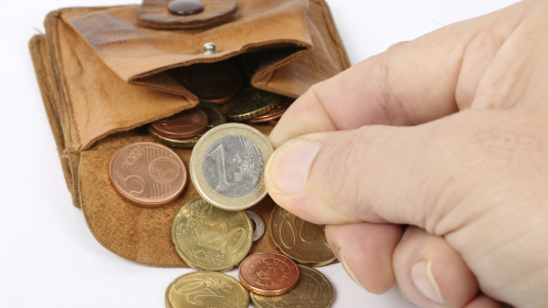 Eine ausgekippte Geldbörse aus der Münzen fallen und eine Hand nimmt einen Euro
