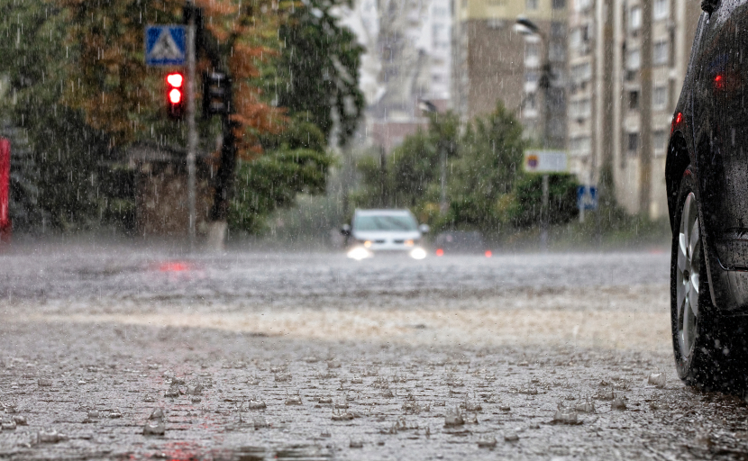 Starregen prasselt auf eine überflutete Straßen. In großer Entfernung sieht man ein Auto im Wasser entgegenkommen