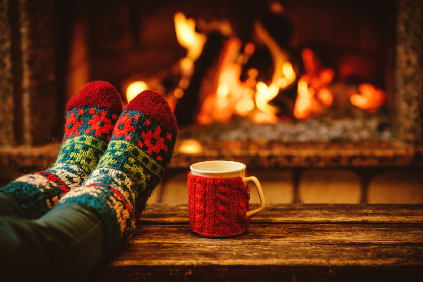 Zwei Füße mit Weihnachtssocken auf einem Tisch dahinter ein Kaminfeuer