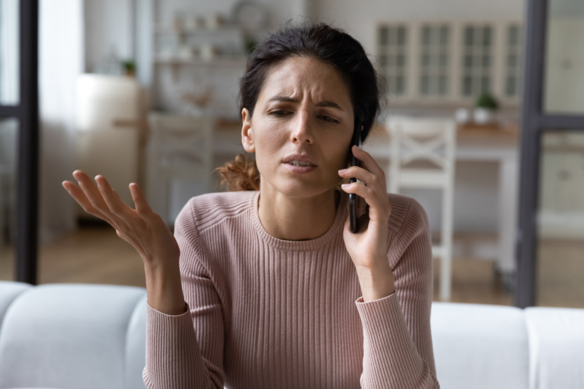 Frau telefoniert im Wohnzimmer, Gestik und Mimik wirken verärgert