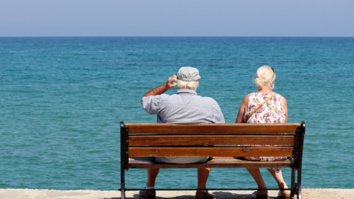 Älteres Paar sitzt auf einer Holzbank und blickt aufs Meer, Rückansicht.