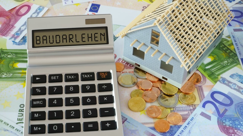 Modellhaus und Taschenrechner mit dem Wort Baudarlehen auf dem Display auf Euro-Scheinen