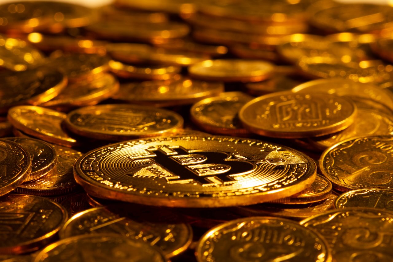 Gold Kryptowährung Bitcoin vor dem Hintergrund vieler anderer Goldmünzen in hartem Licht. Neues Konzept des steigenden Wertes der digitalen Kryptowährungen der Blockchain-Branche. Nahaufnahme.