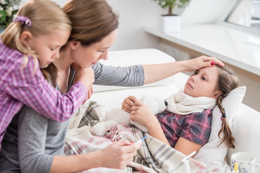 Mutter sitzt am Krankenbett der kranken Tochter und misst die Temperatur