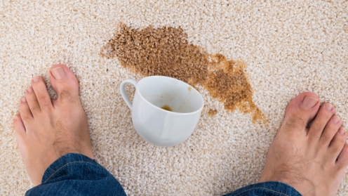 Mann steht vor einer kaffeetasse, in der nähe von kaffee verschüttet auf teppich