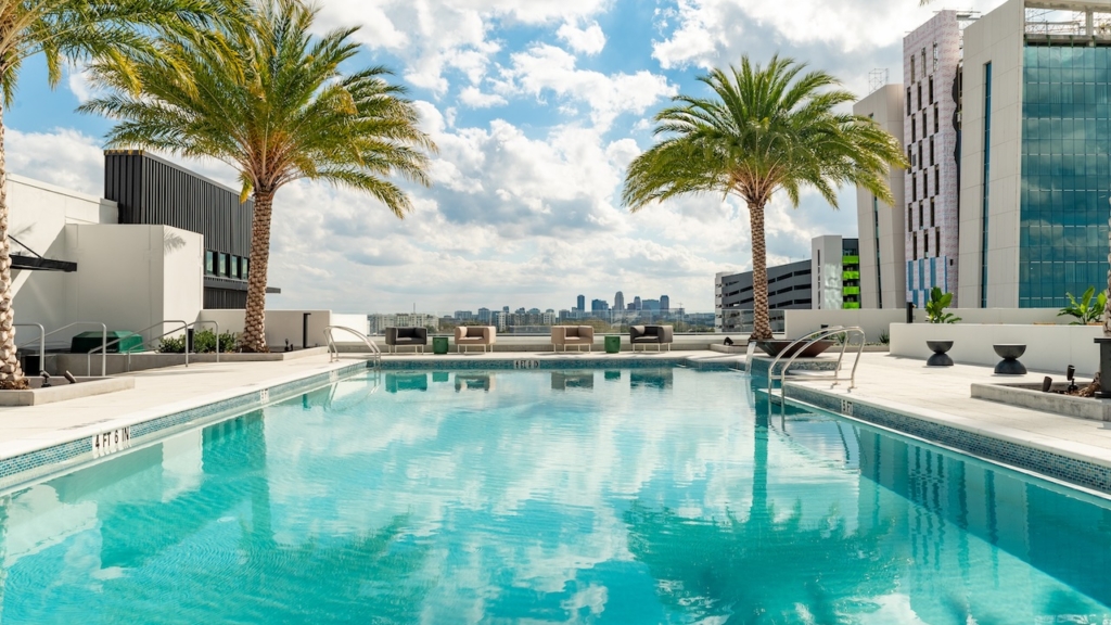 Blick über einen Pool mit Palmen auf eine Stadt