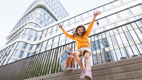 Two girls firends jumping down from concrete wall in city. Low angle view.